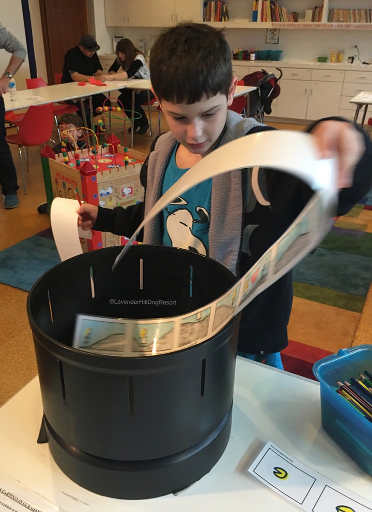 A boy inside the museum viewing an animated cartoon strip inside a zoetrope.